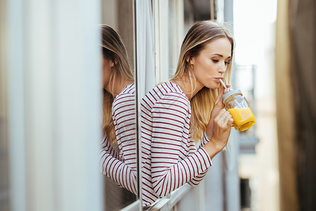 年轻女子喝着一杯天然橙汁 从家窗外倾斜而下 从家里走出来水果食物稻草女孩黑发果汁快乐头发橙子饮食玻璃高清图片素材