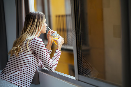 年轻女子喝着一杯天然橙汁 从家窗外倾斜而下 从家里走出来果汁食物水果头发成人快乐女孩黑发女性玻璃橙子高清图片素材