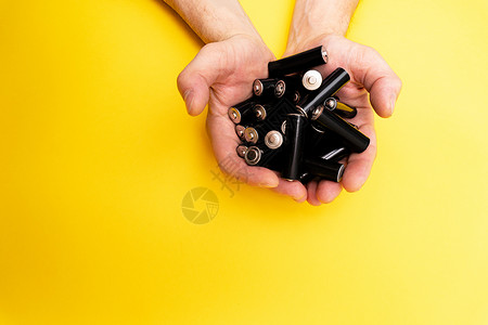有很多黑AA电池 在男性手中 黄色背景的背景图片