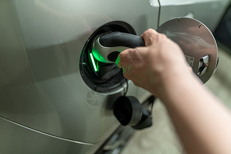 油箱盖在一个人的手上的详细视图是插入充电线并插入他的电动汽车燃料盖 绿灯表示活性碳化过程背景