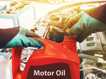 机油润滑油机械师打开红色加仑马机油的盖子 以在修理车间重新装满汽车发动机背景