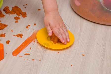 儿童用手把橙色沙子压成一个模具 用于玩具松饼和米木桌上的蛋糕运动沙箱盘子橙子练习造型幼儿园黄色勺子创造力背景图片