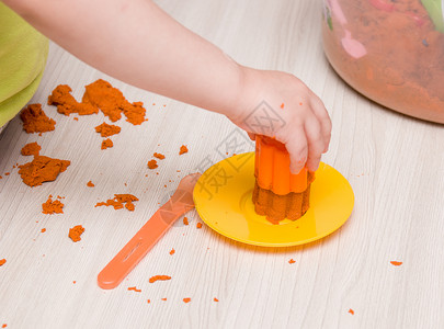 儿童用手把橙色沙子压成一个模具 用于玩具松饼和米木桌上的蛋糕创造力练习沙箱烹饪勺子t恤爱好造型手指男生背景图片
