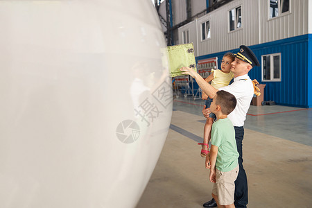 飞机部件身着制服的专业飞行员向他的两个小孩展示飞机的部件 他们来飞机库看望他们的父亲背景