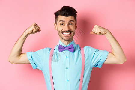 带着领领带和吊带微笑的caucasian男子 展示肌肉和感觉强健 有弹性的二头肌以炫耀 站在粉红色背景上胡须快乐促销男人广告吊带背景图片