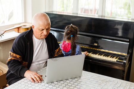 小女孩和爷爷一起弹钢琴 在笔记本电脑上学习细绳竞赛作曲家课堂教育闲暇男人孩子学校网课背景图片