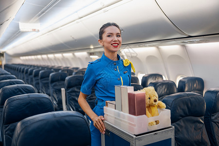 身穿亮蓝色制服 性格开朗的女空姐对着镜头微笑 同时带着礼物穿过空荡荡的飞机过道背景图片