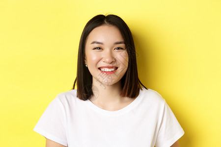 美人 紧贴着笑笑可爱的亚洲女人 完美的白微笑牙齿和发光皮肤 穿着T恤站在黄色背景上情感快乐商业学生工作室女孩手势黑发促销成人背景图片