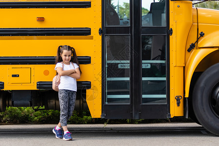 在黄色校车附近有背背包女孩的黄色校车快乐驾驶路线知识公共汽车微笑教育女学生小学生学习背景图片