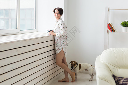 穿着舒适家庭衬衫的女人在家放松 玩狗杰克拉塞尔特瑞尔 喝茶 早安概念猎犬衣服杯子羊毛房子拖鞋女士宠物皮肤女性背景图片
