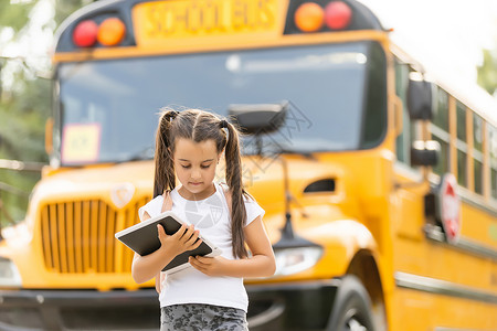 在黄色校车附近有背背包女孩的黄色校车学生快乐笔记本路线小学生童年学习补给品汽车微笑背景图片