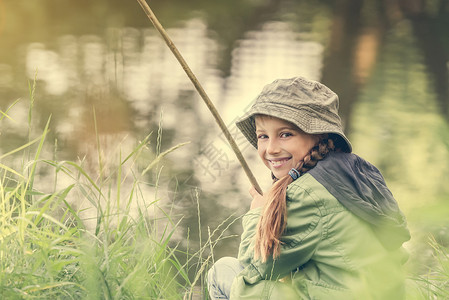 坐着钓鱼女孩小女孩笑着微笑的小鱼女孩青年假期钓鱼童年池塘娱乐孩子乐趣外套帽子背景
