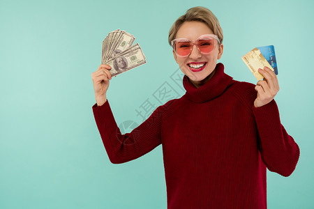 美元代金券微笑的caucasian女人的肖像 持有信用卡和我们美元的钱 而看着被蓝色背景隔绝的相机背景