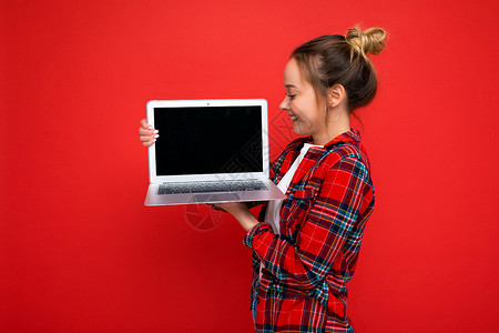 身穿红衬衫 被红色墙背景隔绝的银幕上观看屏幕的迷人年轻女士持网本的侧侧面简介照片神器电子监视器电脑互联网技术空间小样笔记本背景图片