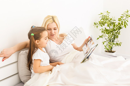 母亲和女儿在床上看一本照片书艺术卧室邻家照片房间女孩女性专辑房子摄影背景图片
