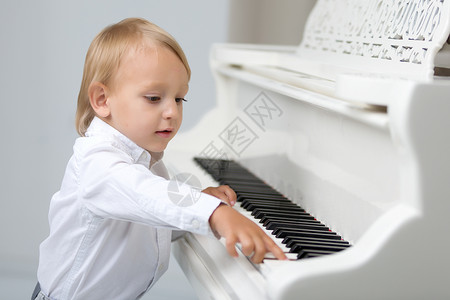钢琴男生素材画室里的小孩 在白色钢琴附近歌曲教育男生幼儿园学习微笑学校乐趣音乐钢琴家背景