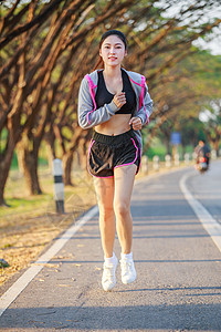 在公园中运行的健身妇女娱乐赛跑者女性慢跑者女士训练运动运动装树木街道背景图片