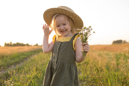 暖男型动毛笔字一个戴着草帽的金发小女孩拿着一束雏菊走在田野里 走在自然 自由和生态友好型生活方式中的概念童年植物喜悦女孩帽子环境金发女郎野生动背景