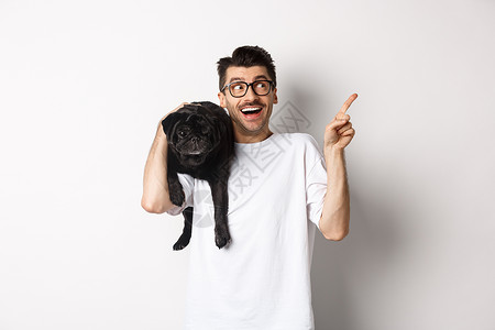 宠物宣传展架戴着眼镜的帅帅壮男子 肩上抓着可爱的黑小狗 用宣传标志指向右上角 站在白色背景之上行动朋友犬类乐趣微笑动物潮人横幅男性宠物背景
