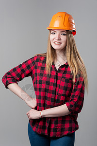 橙色格子一个年轻有魅力的女人的肖像 头戴橙色头盔金发 穿着中性灰色背景的金发安全帽帽子建筑学经理工作工程头发工程师金发女郎成人背景