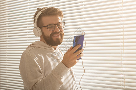 年轻时髦的嬉皮士男子在智能手机中选择最喜欢的音乐和办公室耳机的近距离肖像 Music订阅概念思维窗户个性衬衫商业职业冒充工作经理背景图片