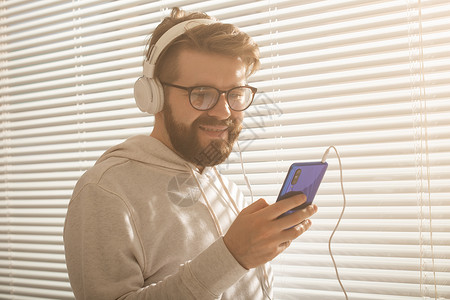 年轻时髦的嬉皮士男子在智能手机中选择最喜欢的音乐和办公室耳机的近距离肖像 Music订阅概念衬衫工作职业冒充男性商业企业家个性智背景图片