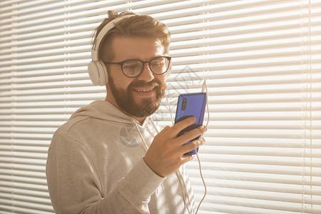年轻时髦的嬉皮士男子在智能手机中选择最喜欢的音乐和办公室耳机的近距离肖像 Music订阅概念个性商业男人衬衫潮人企业家经理领导者背景图片