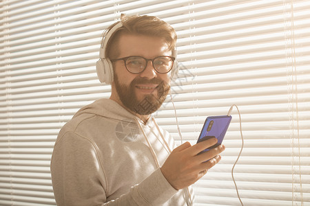年轻时髦的嬉皮士男子在智能手机中选择最喜欢的音乐和办公室耳机的近距离肖像 Music订阅概念经理智力衬衫个性男人潮人思维冒充男性背景图片