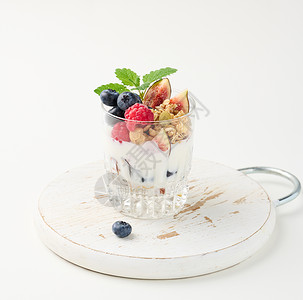 格兰云天透明玻璃 加花粉和酸奶 在成熟的草莓 蓝莓和白桌上的无花果上浇注覆盆子水果玻璃奶制品粮食蓝色营养早餐桌子食物背景