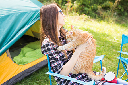 音乐家哈咪猫人 夏季旅游和自然概念     在帐篷附近有猫的年轻妇女女士闲暇旅行女孩荒野蓝色背包女性音乐假期背景