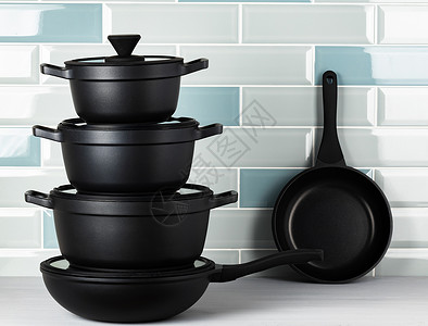 黑色平底锅针对蓝色瓷砖墙的新黑餐具黑色烹饪厨房柜台厨具平底锅炊具背景