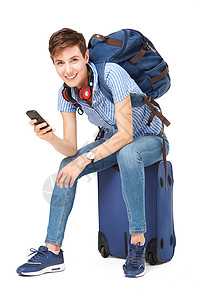 青年妇女坐在手提箱上 手拿着手机旅行享受耳机身体女孩游客背包电话女士行李背景图片