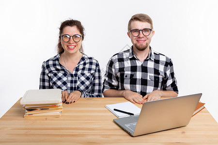 人与教育概念两名身着格格衬衫的学生坐在一张桌子上电脑成人女孩女士极客眼镜笔记本图书男人工作室背景图片