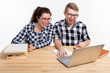 人与教育概念两名身着格格衬衫的学生坐在一张桌子上喜悦成人电脑快乐工作室笔记本女士享受男人图书背景图片