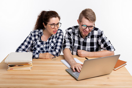 人与教育概念两名身着格格衬衫的学生坐在一张桌子上男人极客工作室喜悦成人电脑享受男性斗争图书背景图片