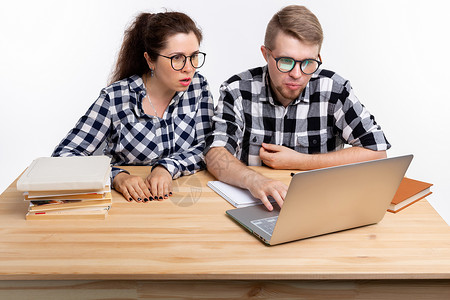人与教育概念两名穿着格格衬衫坐在桌边的令人迷惑的学生女士逗乐男性电脑成人桌子笔记本喜悦夫妻快乐背景图片