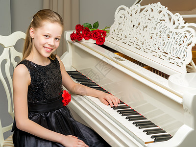 女孩钢琴在钢琴旁边的女学生 弹着一束花朵钥匙学习学生音乐家艺术闲暇孩子裙子音乐乐队背景