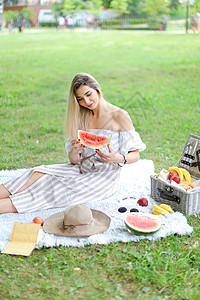 坐在西瓜旁边的女孩女孩坐在水果和帽子旁边的格子上 吃西瓜 本底草背景