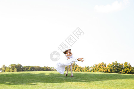 新郎快乐在白天空背景的草地上 抱着新娘背景图片