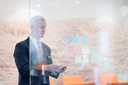 高级商务人士与贴纸一起做计划笔记商务伙伴玻璃战略男人房间办公室人士灰色背景图片