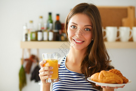 吞噬年轻女人拿着一杯果汁和蛋糕 站在厨房里背景