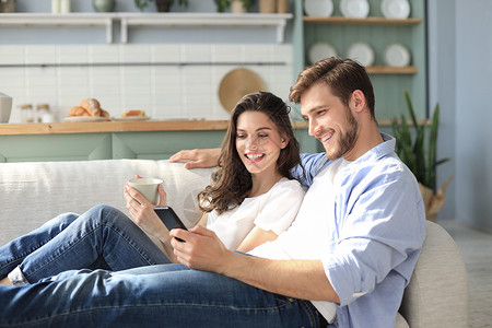 年轻夫妇坐在起居室的沙发上 在智能手机里观看网上内容 笑声租房者男人房间享受游戏电视家庭租户电影女孩背景图片