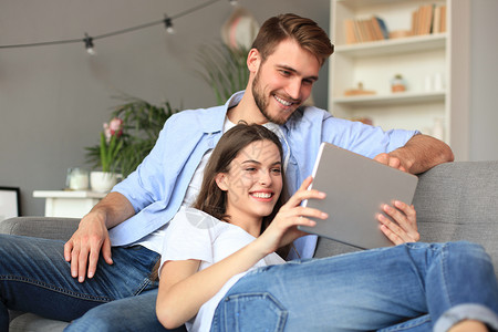 客厅素材网站在客厅沙发上坐着一块平板电脑观看媒体内容的年轻夫妇网站拥抱房子软垫女士女孩男人电视网络电影背景