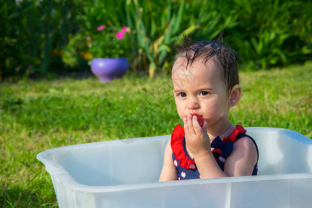 一个女孩在炎热的一天 爬上泳衣 在洗澡和吃草莓背景图片