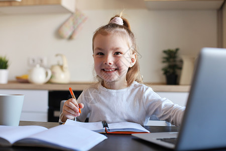 微笑的小女孩在家里使用笔记本电脑在线学习手写 可爱快乐的小孩在 PC 上上互联网课程或课程教育写作休闲白人工作技术网站生活方式音背景图片
