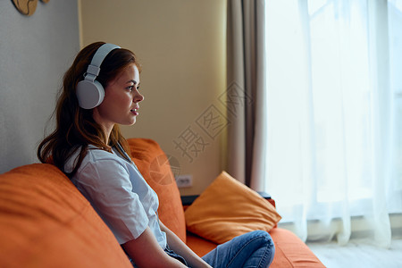 在沙发娱乐节目里 家里的女用耳机肖像成人长椅女性房间喜悦黑发享受音乐快乐微笑背景图片