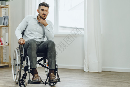 青年残疾男子坐在窗户旁边的轮椅上残障孤独医疗悲伤椅子车辆男性人士退休病人背景图片