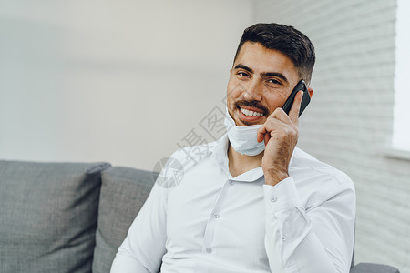 带着面罩的英俊年轻商务人士在电话上说话讲话人士企业家讨论商业商务面具手机男性办公室背景图片