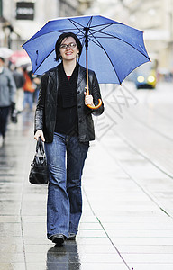 妇女带着雨伞在街上流浪雨量夹克蓝色风暴街道季节购物天气城市下雨背景图片