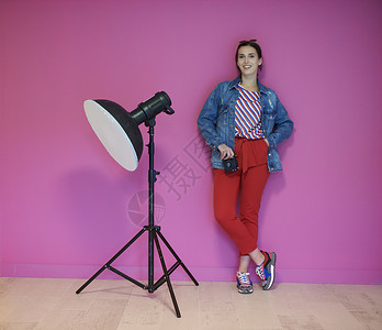 粉红色照相机年轻女士一边靠着粉红色墙 一边拿着照相机倾斜成人技术手电筒相机职业工具女孩冒充工作背景